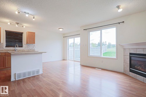 Open-concept living space with wood-finish flooring, a corner fireplace with a tiled surround, and large windows - 1627 Melrose Place Sw, Edmonton, AB - Indoor With Fireplace