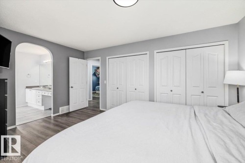 Bedroom featuring wood-finish flooring, two sets of bi-fold closets, and an arched doorway to a bathroom - 3570 Mclean Crescent, Edmonton, AB - Indoor Photo Showing Bedroom