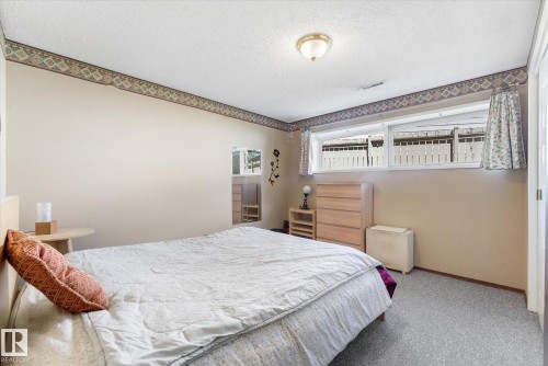 Carpeted bedroom featuring a large window with privacy curtains, textured walls, a decorative border, and a ceiling-mounted light fixture - 886 Knottwood Road S, Edmonton, AB - Indoor Photo Showing Bedroom
