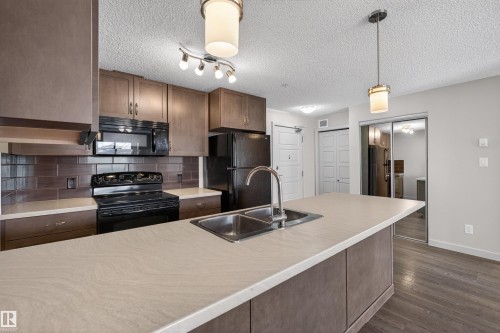 Modern kitchen featuring wood-finish cabinetry, a subway tile backsplash, and a large central island with an undermount double-basin sink - 215 6084 Stanton Drive, Edmonton, AB - Indoor Photo Showing Kitchen With Double Sink