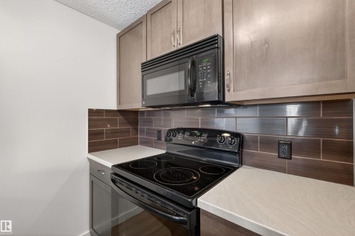 Modern kitchen featuring light gray cabinetry, an over-the-range microwave, and a black electric range - 215 6084 Stanton Drive, Edmonton, AB - Indoor Photo Showing Kitchen