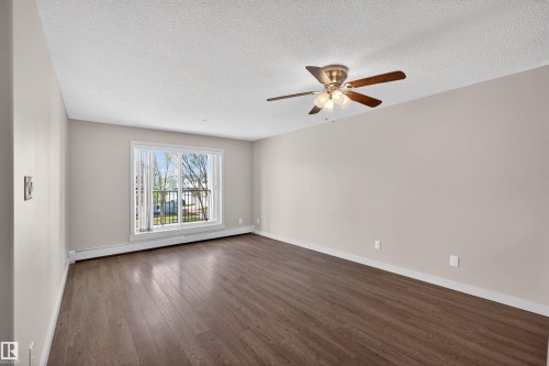 Spacious room featuring wood-finish flooring, a contemporary ceiling fan with lighting, and neutral wall tones - 215 6084 Stanton Drive, Edmonton, AB - Indoor Photo Showing Other Room