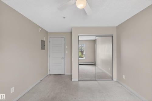 Carpeted interior space featuring a ceiling fan with integrated lighting, a paneled door, and a mirrored closet - 215 6084 Stanton Drive, Edmonton, AB - Indoor Photo Showing Other Room