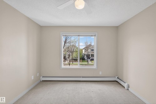 Neutral-toned room featuring a central window, carpet flooring, baseboard heating, and a ceiling fan with integrated lighting - 215 6084 Stanton Drive, Edmonton, AB - Indoor Photo Showing Other Room