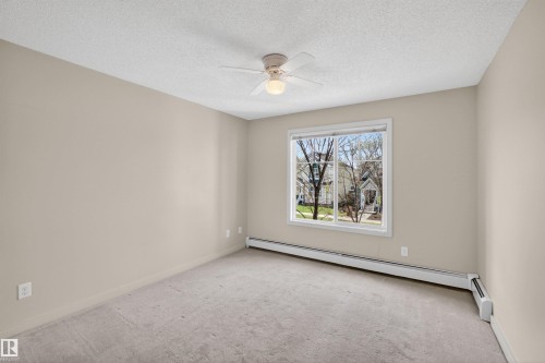 Carpeted room featuring a large window, neutral wall tones, a ceiling fan with integrated lighting, and baseboard heating - 215 6084 Stanton Drive, Edmonton, AB - Indoor Photo Showing Other Room