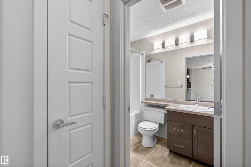 Bathroom featuring a tub/shower combination, dark wood-finish vanity with a single basin, tiled flooring, and a four-light fixture - 215 6084 Stanton Drive, Edmonton, AB - Indoor Photo Showing Bathroom