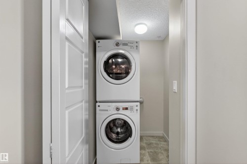 Dedicated laundry area featuring a stacked washer and dryer unit, overhead lighting, and tiled flooring - 215 6084 Stanton Drive, Edmonton, AB - Indoor Photo Showing Laundry Room