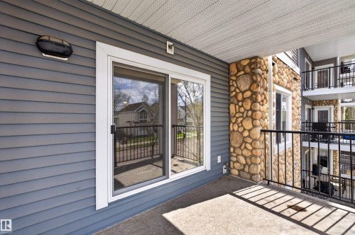 Outdoor patio featuring a sliding glass door entry, stone accent pillar, and black metal railing - 215 6084 Stanton Drive, Edmonton, AB - Outdoor With Balcony With Exterior