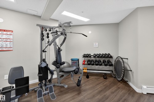 Well-appointed fitness room featuring a multi-station weight machine, dumbbell rack, and wood-finish flooring - 215 6084 Stanton Drive, Edmonton, AB - Indoor Photo Showing Gym Room