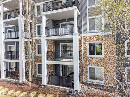 Multi-story condominium exterior featuring stone veneer accents, horizontal siding, multiple private balconies with black railings, and white-framed windows - 215 6084 Stanton Drive, Edmonton, AB - Outdoor With Balcony With Facade