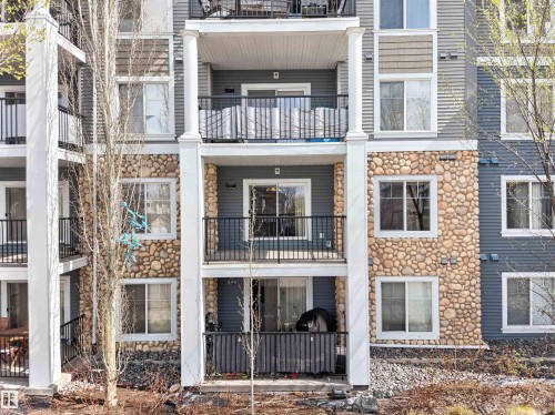 Multi-story residential facade featuring stone veneer accents, white balustrades, and private balconies with black railings - 215 6084 Stanton Drive, Edmonton, AB - Outdoor With Balcony With Facade