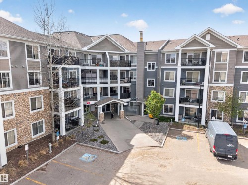 Multi-story residential building featuring a stone and siding exterior, multiple balconies with dark railings, a covered main entrance, and an asphalt parking area - 215 6084 Stanton Drive, Edmonton, AB - Outdoor With Facade