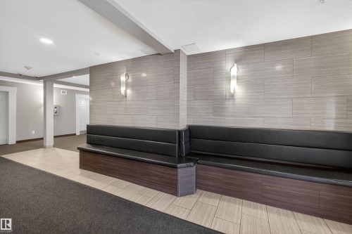 Lobby featuring built-in black seating, textured wall paneling with sconce lighting, and mixed tile and carpet flooring - 215 6084 Stanton Drive, Edmonton, AB - Indoor Photo Showing Other Room