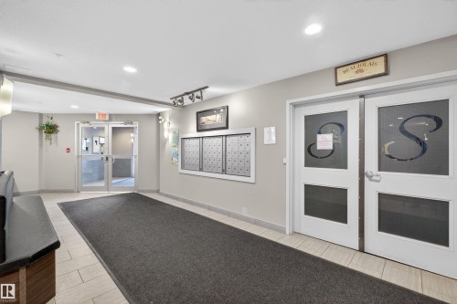 Building entry featuring mailboxes, dual entry doors with frosted panels, and recessed lighting - 215 6084 Stanton Drive, Edmonton, AB - Indoor Photo Showing Other Room With Fireplace