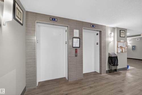 Elevator lobby featuring two elevators with gray tile surrounds and wood-finish flooring - 215 6084 Stanton Drive, Edmonton, AB - Indoor Photo Showing Other Room