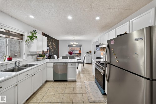 The kitchen features white cabinetry, a double basin sink, stainless steel appliances, and tiled flooring - 3517 25 Street, Edmonton, AB - Indoor Photo Showing Kitchen With Double Sink