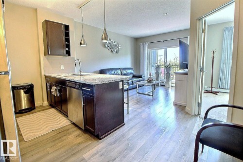 Open-concept living space featuring wood-finish flooring, a kitchen island with stone countertop, stainless steel appliances, and a sliding glass door leading to an exterior balcony - 327 508 Griesbach Parade, Edmonton, AB - Indoor