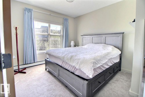 Carpeted bedroom with a large window, baseboard heating, and light-colored walls - 327 508 Griesbach Parade, Edmonton, AB - Indoor Photo Showing Bedroom