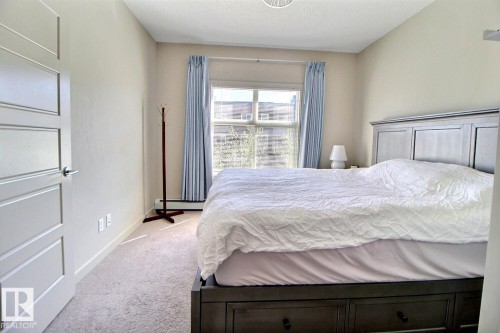 Neutral-toned room with light-colored carpeting and a window featuring light blue drapes - 327 508 Griesbach Parade, Edmonton, AB - Indoor Photo Showing Bedroom