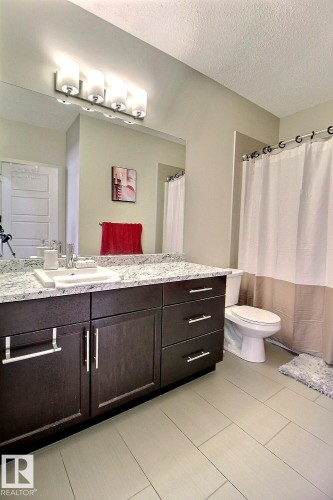 Bathroom featuring a dark wood-finish vanity with ample storage, a light-toned countertop, a full-width mirror, and a modern four-light fixture - 327 508 Griesbach Parade, Edmonton, AB - Indoor Photo Showing Bathroom