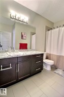 Bathroom featuring a dark wood-finish vanity with ample storage, a light-toned countertop, a full-width mirror, and a modern four-light fixture - 