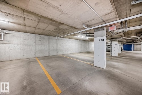 Parking garage featuring concrete walls, concrete flooring with painted yellow lines, and exposed overhead piping - 327 508 Griesbach Parade, Edmonton, AB - Indoor Photo Showing Garage