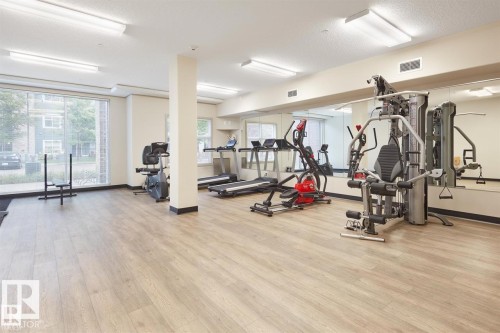 Fitness room featuring wood-finish flooring, mirrored wall, large windows, and overhead fluorescent lighting - 327 508 Griesbach Parade, Edmonton, AB - Indoor Photo Showing Gym Room