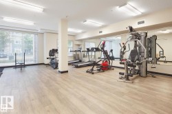Fitness room featuring wood-finish flooring, mirrored wall, large windows, and overhead fluorescent lighting - 