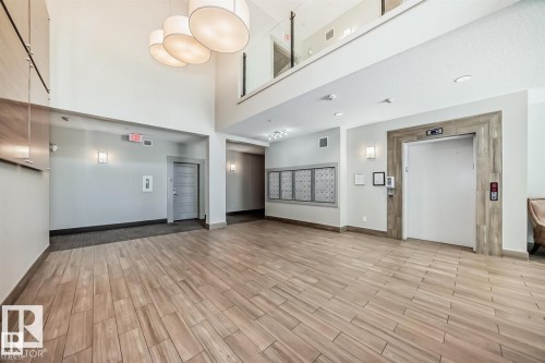 Spacious lobby featuring wood-finish flooring, high ceilings, and contemporary pendant lighting - 327 508 Griesbach Parade, Edmonton, AB - Indoor Photo Showing Other Room