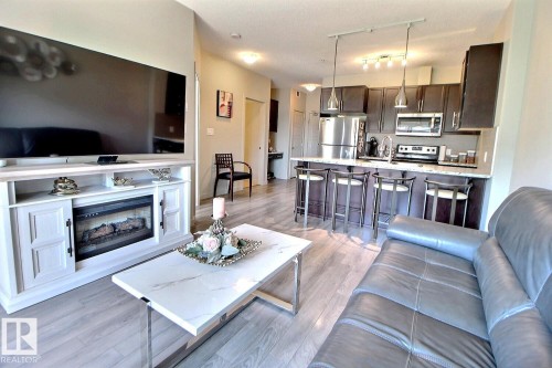 Open-concept living area featuring wood-finish flooring, a kitchen with dark cabinetry, stainless steel appliances, and a breakfast bar with pendant lighting - 327 508 Griesbach Parade, Edmonton, AB - Indoor