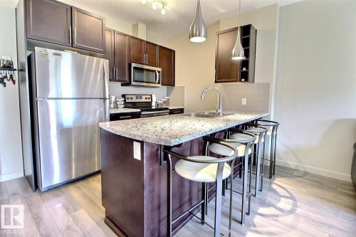 Kitchen featuring an expansive island with a granite countertop, undermount sink, and pendant lighting - 327 508 Griesbach Parade, Edmonton, AB - Indoor Photo Showing Kitchen With Stainless Steel Kitchen With Double Sink With Upgraded Kitchen