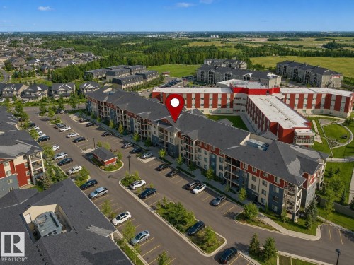 Multi-story residential complex featuring red and gray facades, balconies, and extensive surface parking - 422 5816 Mullen Place, Edmonton, AB -  With View