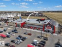 Commercial retail building featuring a large parking lot, red accents, and multiple entrances - 422 5816 Mullen Place, Edmonton, AB  - Outdoor With View 