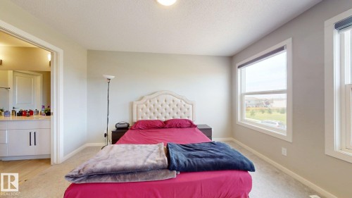 This property offers a bedroom with light-colored walls and carpeting, featuring a tufted headboard and two windows with blinds - 607 31 Avenue, Edmonton, AB - Indoor Photo Showing Bedroom