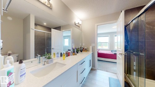 The bathroom features a double vanity with ample counter space, a large mirror, and a shower with a glass enclosure and dark tile surround - 607 31 Avenue, Edmonton, AB - Indoor Photo Showing Bathroom