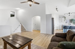 Spacious open-concept living area featuring light wood-finish flooring, vaulted ceilings, and a ceiling fan with integrated lighting - 