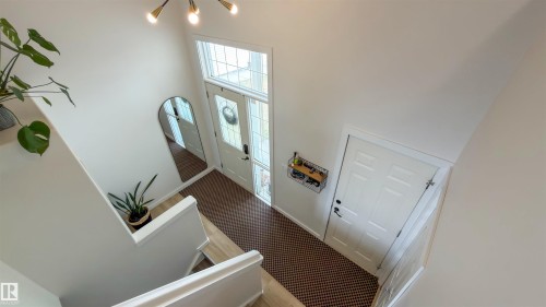 Two-story entry foyer featuring a leaded glass transom and sidelights, a modern chandelier, wood-finish flooring, and a paneled interior door - 396 Kananaskis Way, Devon, AB - Indoor Photo Showing Other Room