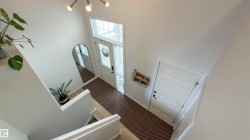 Two-story entry foyer featuring a leaded glass transom and sidelights, a modern chandelier, wood-finish flooring, and a paneled interior door - 