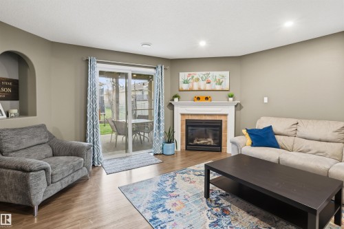 Living space featuring wood-finish flooring, a corner fireplace with a white mantel and tile surround, and a sliding glass door providing access to an outdoor patio - 396 Kananaskis Way, Devon, AB - Indoor Photo Showing Living Room With Fireplace