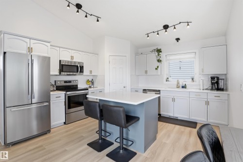 Modern kitchen featuring stainless steel appliances, light wood-finish flooring, white cabinetry with gold-tone hardware, a center island with countertop seating, and track lighting - 396 Kananaskis Way, Devon, AB - Indoor Photo Showing Kitchen