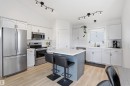Modern kitchen featuring stainless steel appliances, light wood-finish flooring, white cabinetry with gold-tone hardware, a center island with countertop seating, and track lighting - 396 Kananaskis Way, Devon, AB  - Indoor Photo Showing Kitchen 
