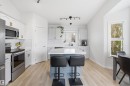 Bright kitchen featuring a central island, stainless steel appliances, light-toned wood-finish flooring, white cabinetry with gold-finish hardware, and track lighting - 396 Kananaskis Way, Devon, AB  - Indoor Photo Showing Kitchen 