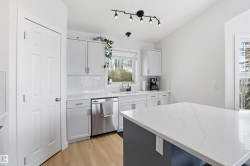 Modern kitchen featuring light cabinetry, stainless steel appliances, wood-finish flooring, a white subway tile backsplash, and a large central island with a solid surface countertop - 