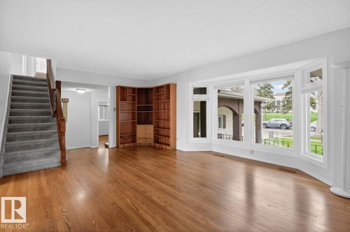 Spacious living area featuring polished wood-finish flooring and a prominent bay window - 8911 84 Avenue, Edmonton, AB - Indoor
