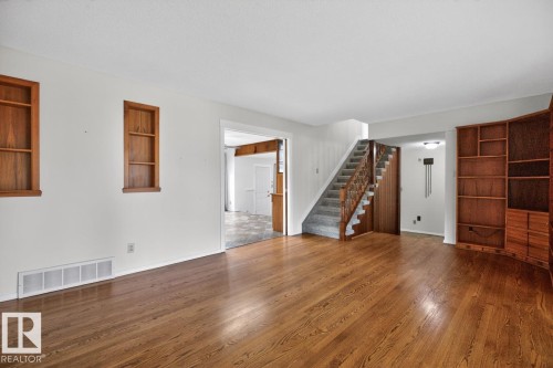 Spacious interior featuring wood-finish flooring, white walls, built-in shelving, and a carpeted staircase with wood banisters - 8911 84 Avenue, Edmonton, AB - Indoor Photo Showing Other Room