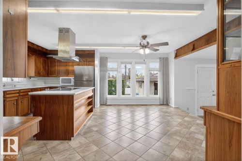 Kitchen and dining area featuring wood cabinetry, a central island with integrated cooktop, stainless steel appliances, and tile flooring - 8911 84 Avenue, Edmonton, AB - Indoor Photo Showing Kitchen