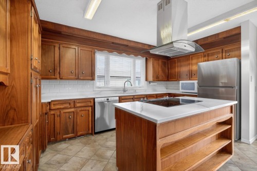 Kitchen featuring an expansive wood-finish cabinetry system with ample storage, a central island with a built-in cooktop, and a sleek stainless-steel range hood - 8911 84 Avenue, Edmonton, AB - Indoor Photo Showing Kitchen