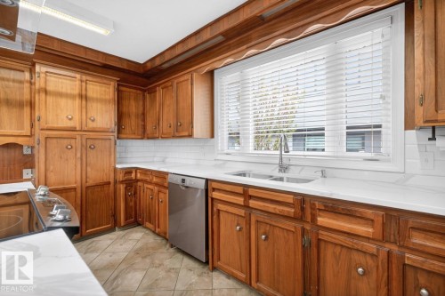 Kitchen featuring wood cabinetry, white subway tile backsplash, light-toned countertops, a stainless steel dishwasher, and a dual-basin sink with a gooseneck faucet - 8911 84 Avenue, Edmonton, AB - Indoor Photo Showing Kitchen With Double Sink