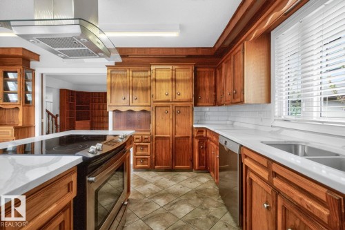 Kitchen featuring wood cabinetry, white countertops, stainless steel appliances, a tile backsplash, and tile flooring - 8911 84 Avenue, Edmonton, AB - Indoor Photo Showing Kitchen With Double Sink