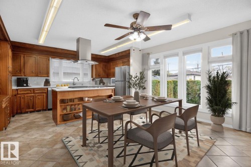 Open-concept kitchen and dining area featuring wood cabinetry, stainless steel appliances, a center island with open shelving, tile flooring, and multiple windows - 8911 84 Avenue, Edmonton, AB - Indoor